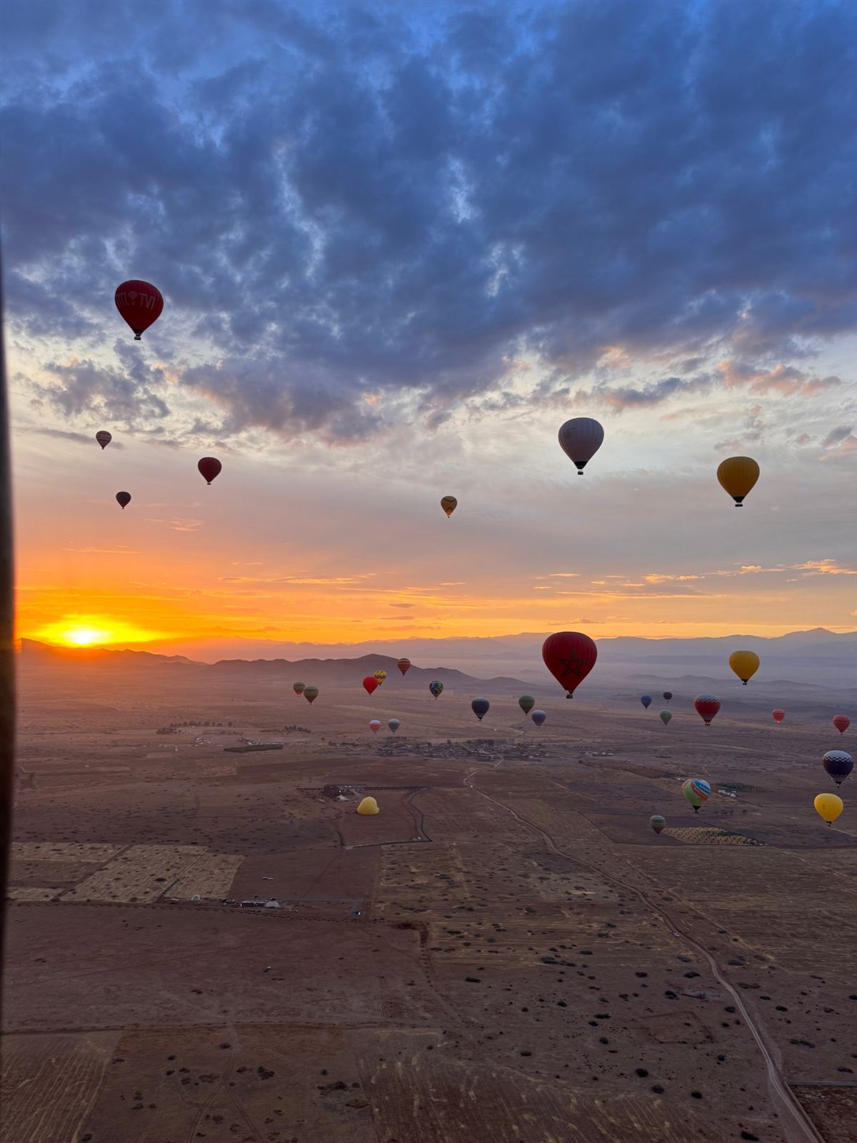 Hot air balloons over the Marrakech countryside at sunrise, with the Atlas Mountains behind